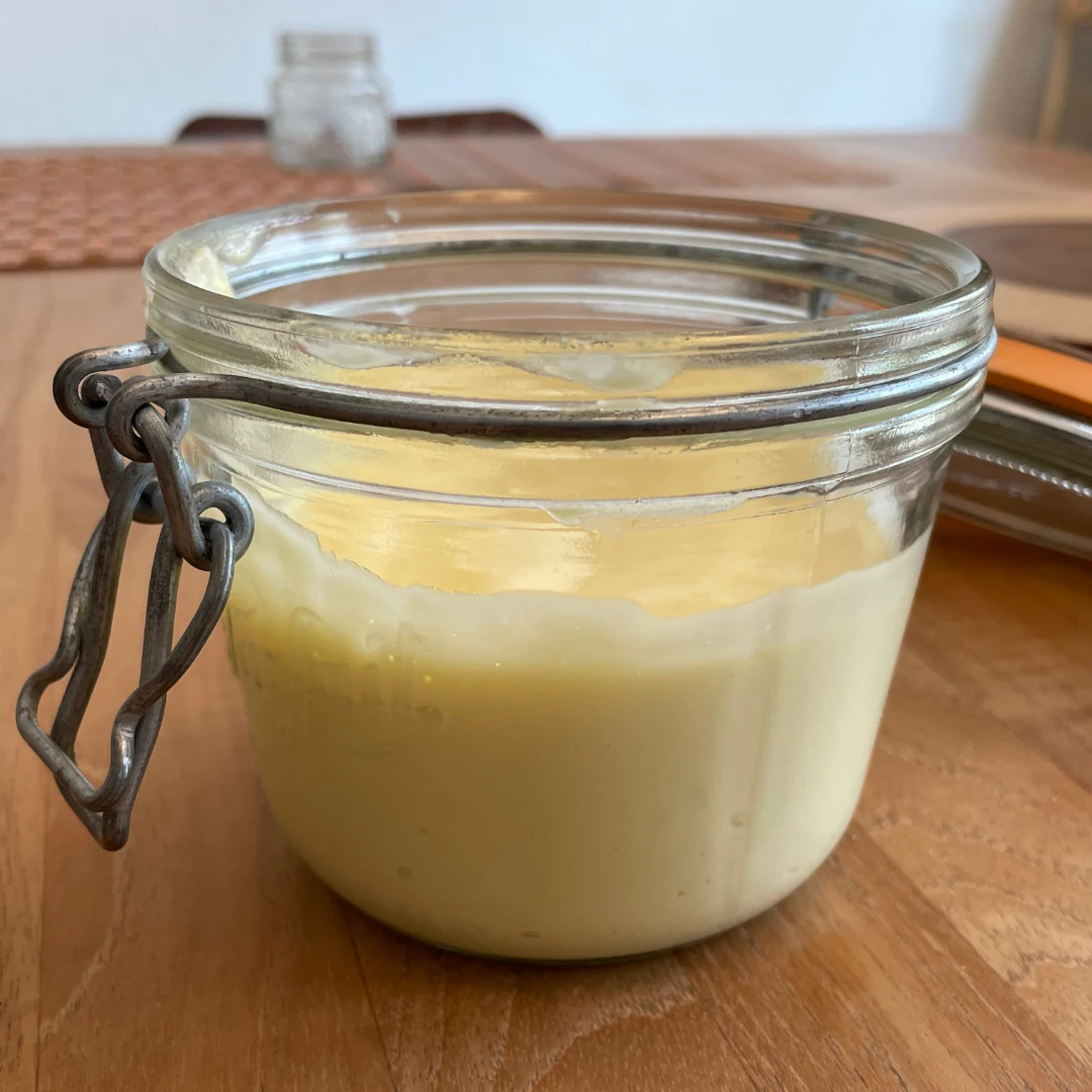 Wide-mouth glass jar of homemade avocado oil mayo with a spoon resting on top