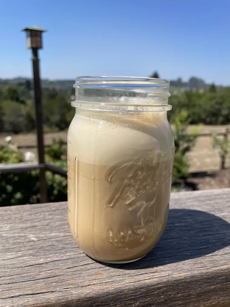 A warm coffee latte in a small cup, frothed pale and creamy with homemade cashew milk — the same technique that makes the yerba mate version