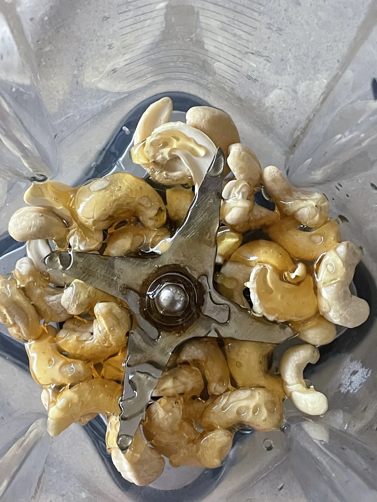Overhead view into a Vitamix blender of raw cashews in honey and water, ready to blend with hot brewed liquid for a single-serving cashew milk latte