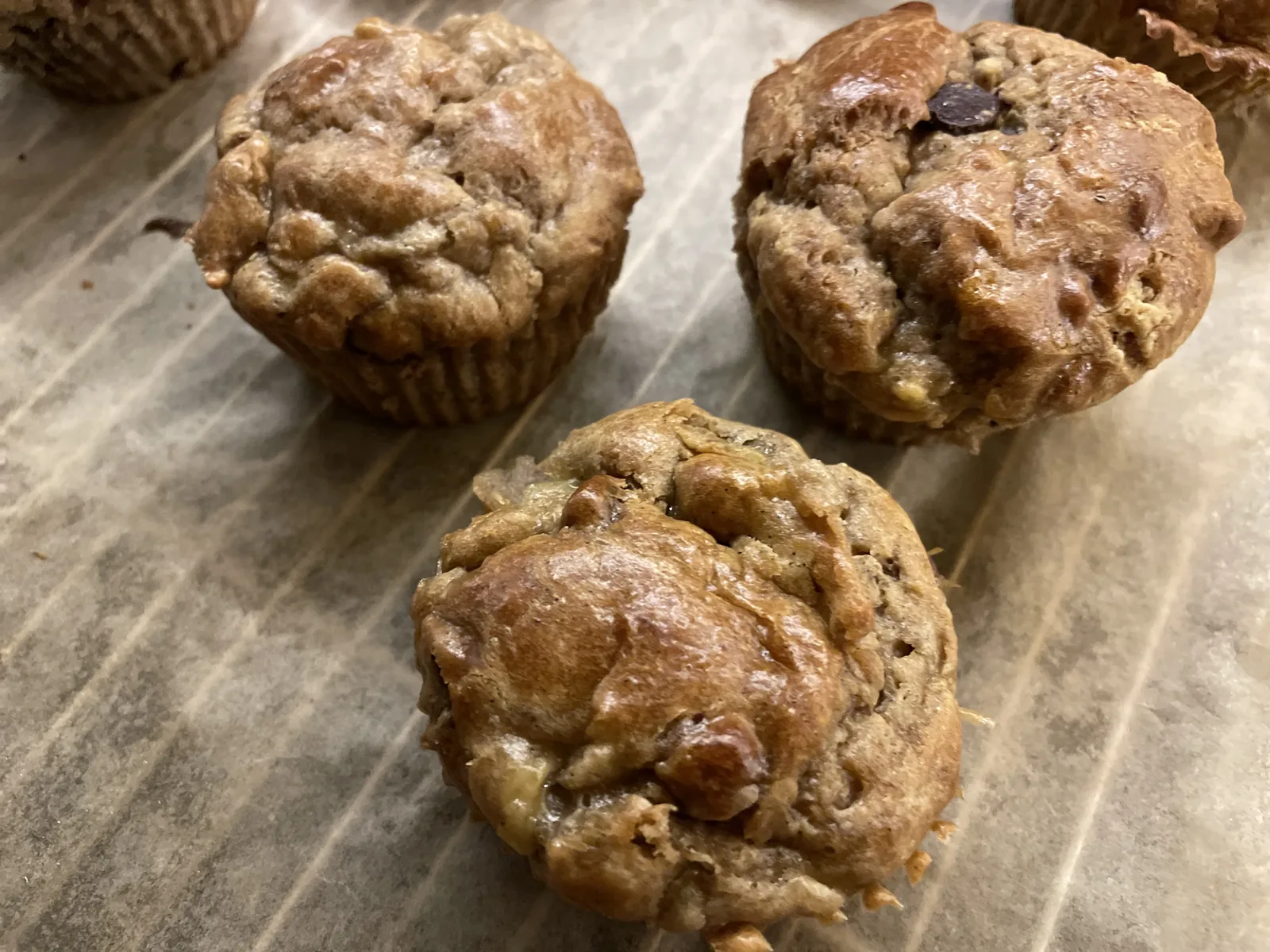 A dozen golden flourless muffins on a wire rack, studded with blueberries and slices of ripe banana, one cut open to show the soft cashew-butter crumb