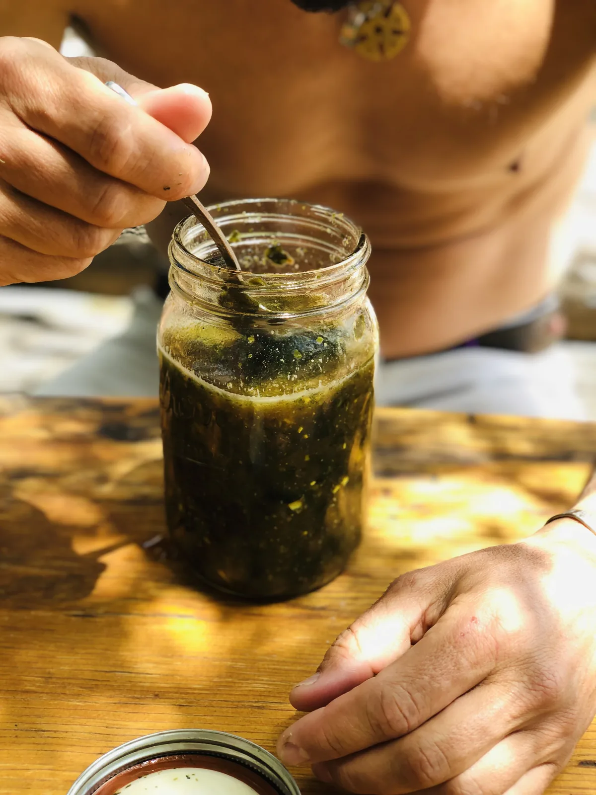 My husband holding a mason jar of assembled bone broth soup, stirring it before drinking, outdoors
