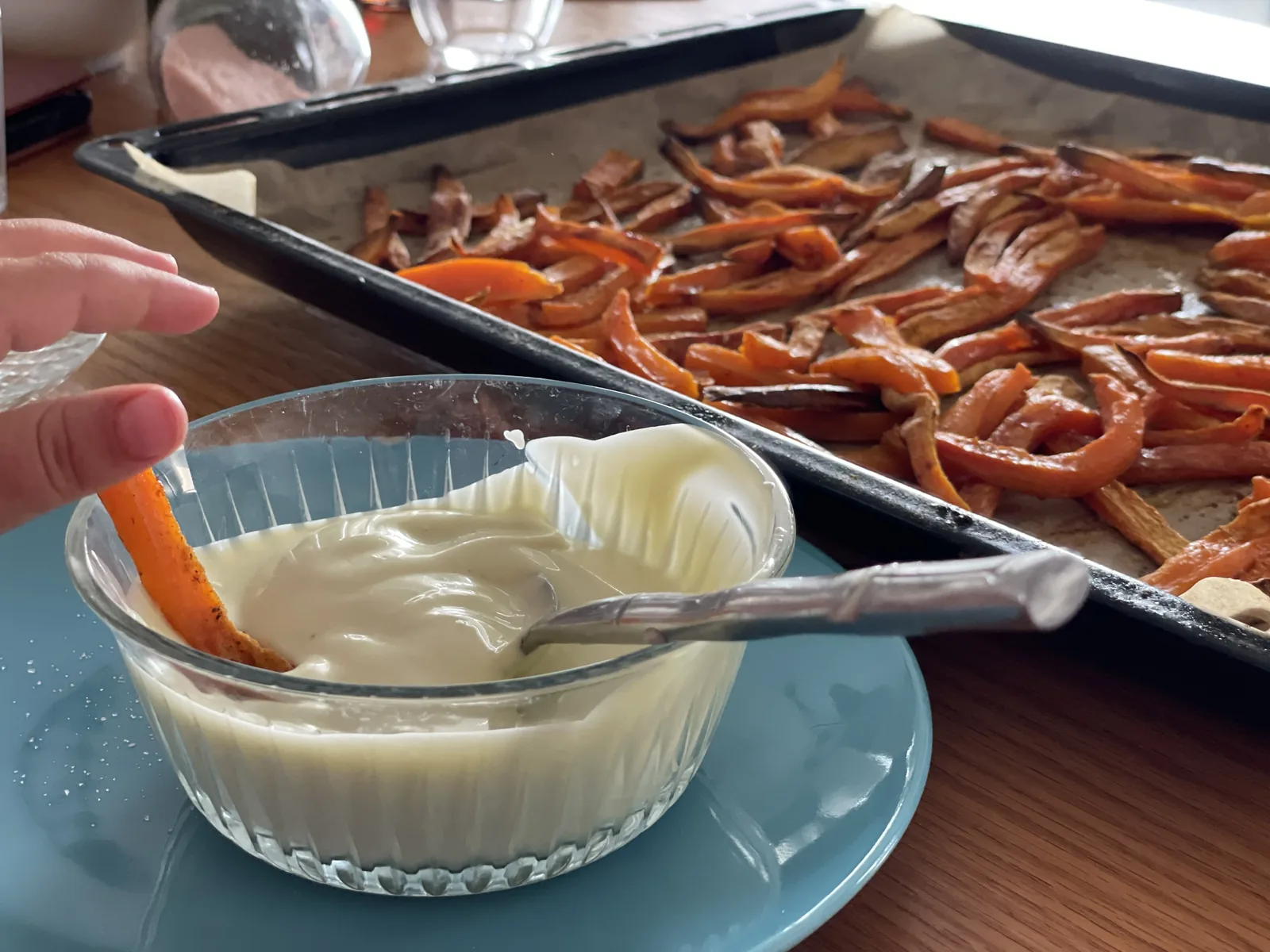 A tray of finished sweet potato chips on parchment with a small bowl of homemade avocado oil mayo on the side for dipping