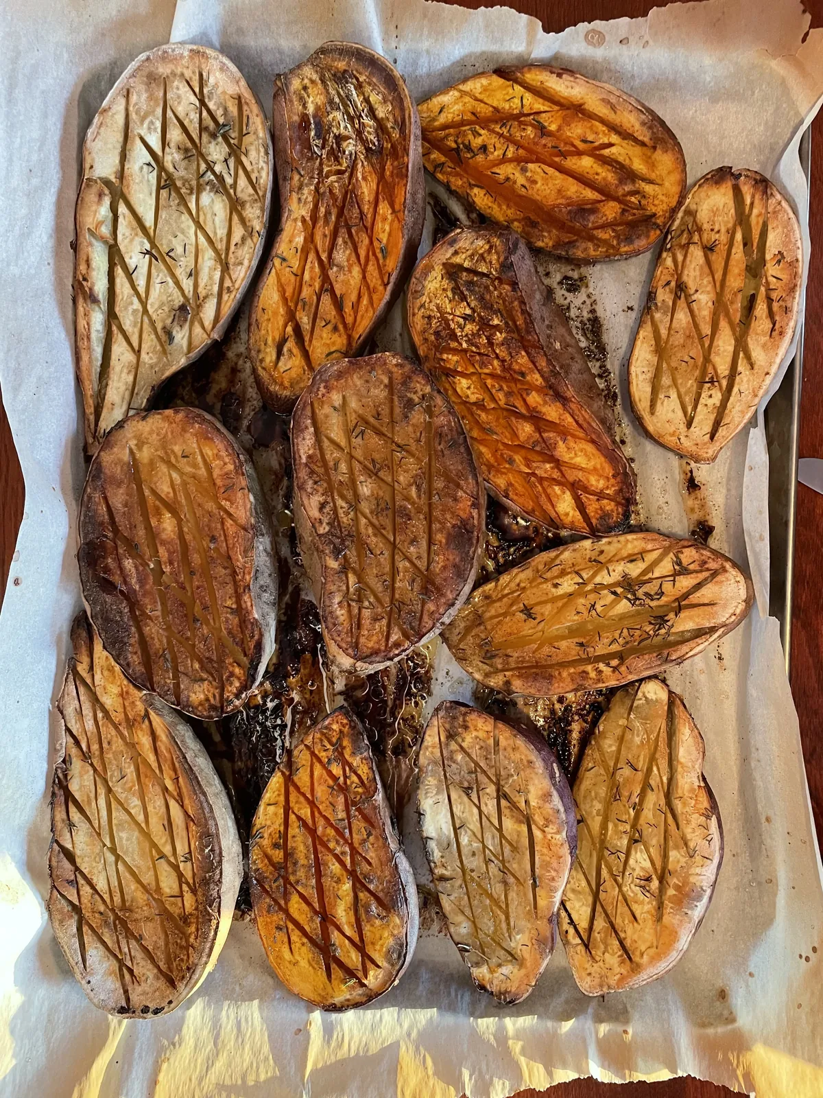 Halved roasted sweet potatoes on parchment paper, deeply caramelized with olive oil and rosemary