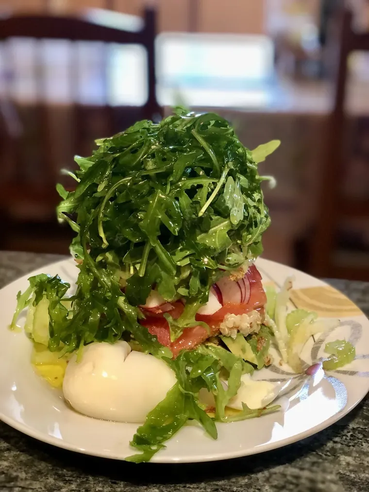 Lunch bowl with soft-boiled eggs cut in half over arugula and baby kale, with kraut, pumpkin seeds, avocado, and a drizzle of olive oil